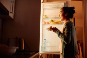 A woman stands in front of an open refridgerator in the evening